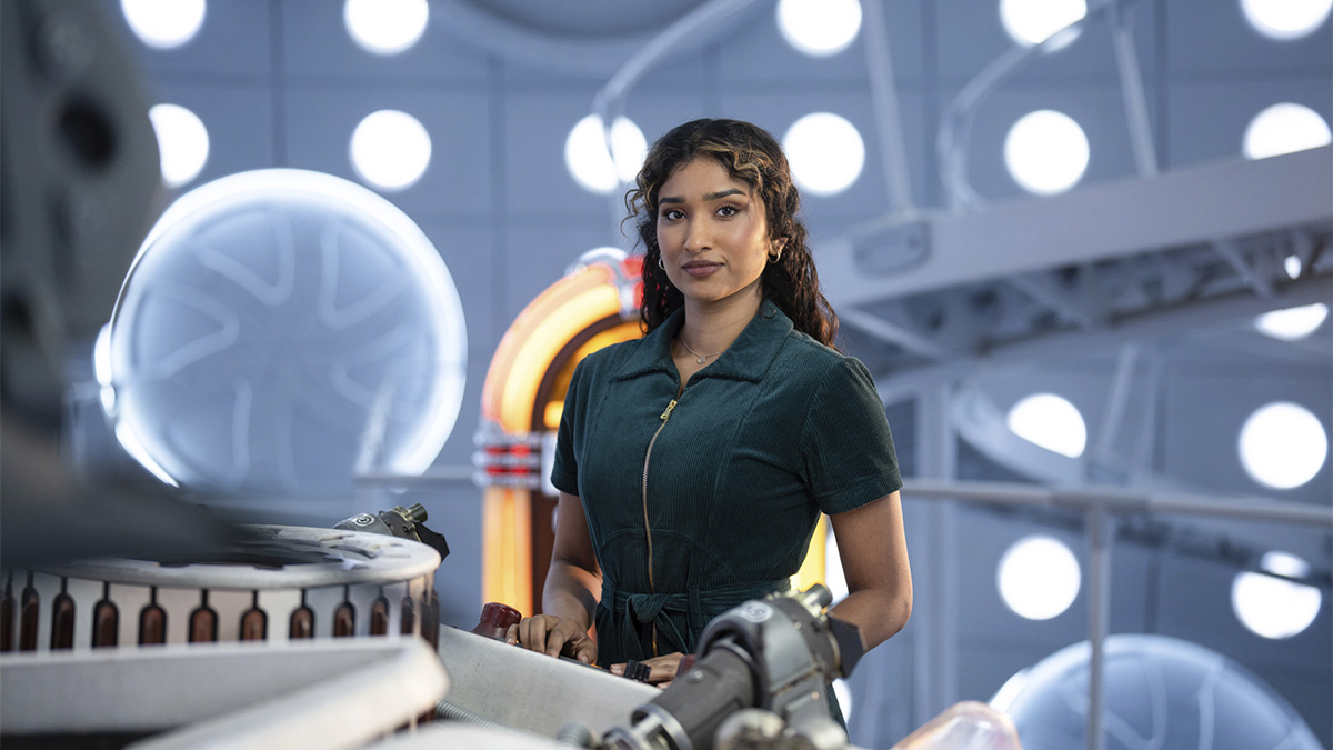 A woman in a green jumpsuit standing by the TARDIS console in Doctor Who